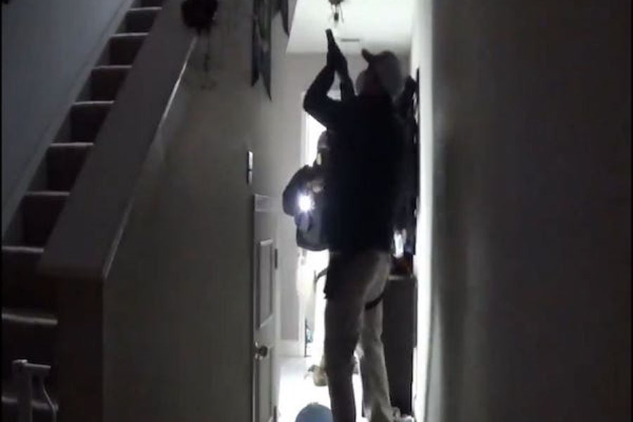 A police officer wields a gun and calls for Rebekah Jones' husband to come downstairs. Photo credit: Rebekah Jones/Twitter.