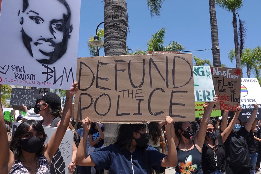 People hold signs during peaceful Black Lives Matter protest march, one of many in San Diego County. One sign reads Defund Police.