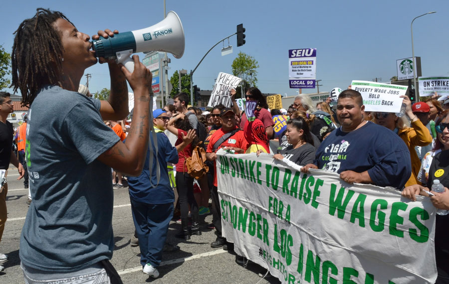 A man shouts into a megaphone at protestors holding a banner advocating raising the minimum wage during a demonstration in Los Angeles. File photo: Dan Holm, Shutterstock.com, licensed.